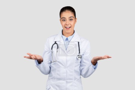 Photo for A surprised happy european lady doctor in a white coat with a stethoscope gestures with her hands open, expressing uncertainty or weighing options in a healthcare setting - Royalty Free Image