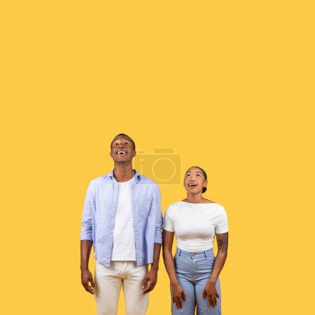 Photo for Black man and woman look upwards with expressions of hope and aspiration, standing against yellow background, place for advertisement, banner - Royalty Free Image