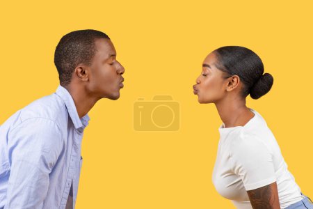 Téléchargez les photos : Vue du profil d'un jeune couple noir qui rondelle pour s'embrasser, les lèvres presque touchantes, sur fond jaune vif, illustrant l'intimité - en image libre de droit