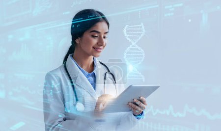 Foto de Tecnología CRISPR. Joven médica india avanzada disfrutando de tecnologías médicas futuristas, estudiando el ADN humano virtual en tabletas digitales, fondo de estudio azul - Imagen libre de derechos