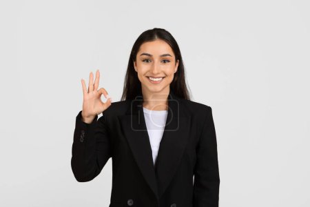 Téléchargez les photos : Joyeux jeune femme d'affaires européenne donnant un geste de main OK pour signifier l'approbation ou le succès, sur fond de studio gris clair - en image libre de droit