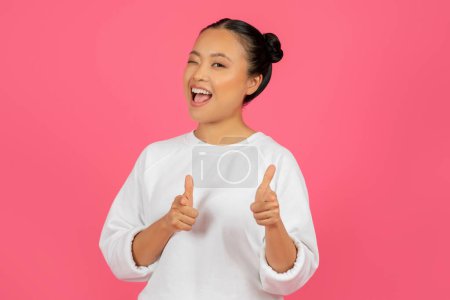 Foto de Joven mujer asiática alegre señalando a la cámara con dos manos y sonriendo, Mujer coreana positiva que indica a alguien, diciendo Gotcha, de pie aislado sobre el fondo del estudio rosa, espacio de copia - Imagen libre de derechos