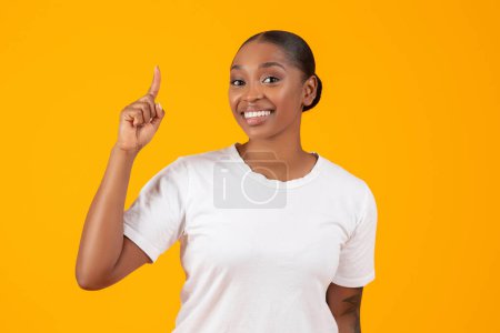 Photo for Inspired happy african american woman gesturing pointing finger up having creative idea over yellow studio backdrop, experiencing inspiration during AHA eureka moment - Royalty Free Image