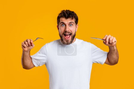 Photo for Im Hungry. Emotional millennial man holding knife and fork ready to eat his dinner, posing looking at camera over yellow studio backdrop. Portrait of funny guy having food cravings - Royalty Free Image