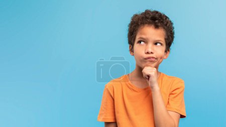 Photo for Pensive young boy with hand on chin, looking up and away at free space in deep thought against soothing blue backdrop, indicating curiosity and contemplation - Royalty Free Image