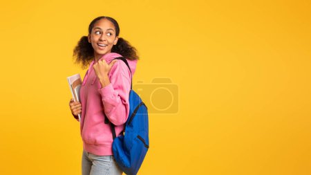 Photo for Young black teen girl with backpack and notebooks posing and smiling on yellow studio backdrop. African American female student ready to start school. Panorama, copy space. Academic education - Royalty Free Image