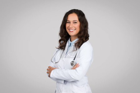 Photo for Portrait of confident female doctor wearing medical white uniform coat and stethoscope, posing with folded arms and smiling isolated on grey studio background - Royalty Free Image