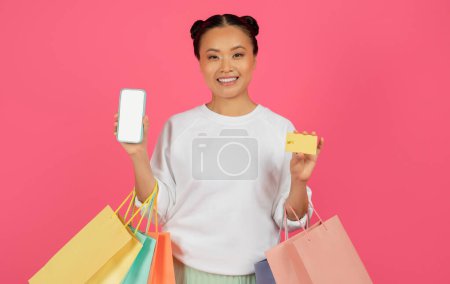 Téléchargez les photos : Shopping App. Happy Asian Lady Holding Smartphone vide, Sacs Shopper et carte de crédit, Souriant Coréen Femme Affichage téléphone portable avec écran blanc vide, Recommander Boutique en ligne, Mockup - en image libre de droit