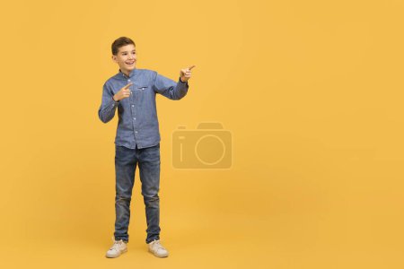 Photo for Nice Offer. Cheerful Teen Boy Pointing Aside At Copy Space With Two Hands, Excited Male Kid Showing Free Place For Advertisement, Standing On Yellow Studio Background, Full Length Shot - Royalty Free Image