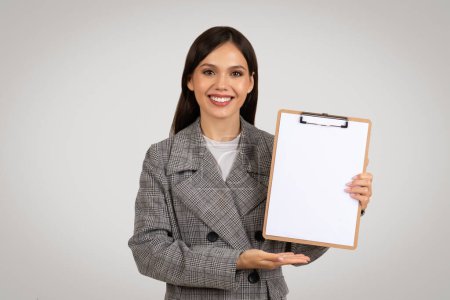 Foto de Mujer profesional en chaqueta houndstooth que muestra portapapeles en blanco, perfecto para mensajes de marketing o contenido personalizado, sobre fondo gris - Imagen libre de derechos