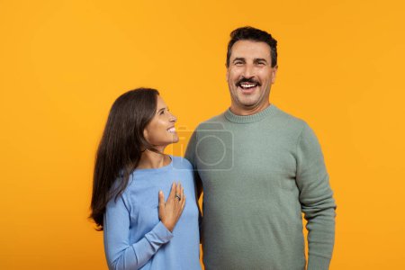 Téléchargez les photos : Une femme et un homme caucasiens joyeux, vêtus de vêtements décontractés, rient avec un fond orange vif, studio. Fun ensemble, style de vie, famille, amour et relation - en image libre de droit