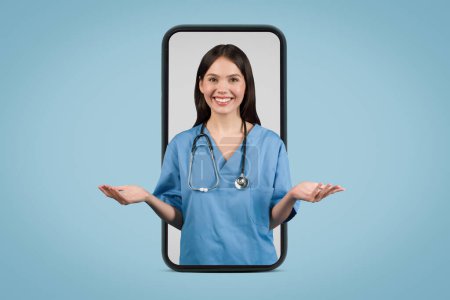 Photo for Young woman nurse in blue coat gesturing at the camera, displayed on smartphone screen, representing an online consultation over a blue background - Royalty Free Image
