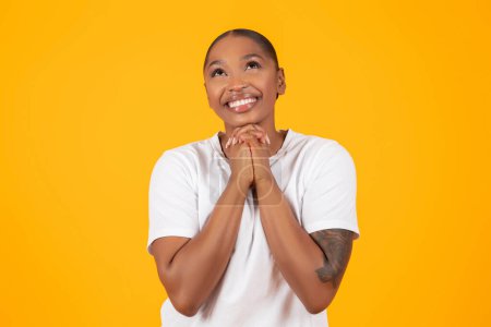 Photo for Portrait Of Happy African American Woman Praying Holding Hands Together With Joyful Expression, Hoping For Best And Asking God Something, Over Yellow Studio Backdrop - Royalty Free Image