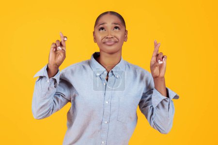 Téléchargez les photos : Dame afro-américaine rêveuse croisant les doigts pour la chance, faisant son vœu chéri, espérant un bon avenir et la fortune sur fond de studio jaune, portrait tourné - en image libre de droit