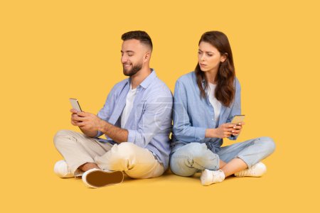 Foto de Hombre y mujer sentados espalda con espalda en el suelo, absortos en sus teléfonos móviles, encarnando la comunicación moderna y el compromiso con las redes sociales - Imagen libre de derechos