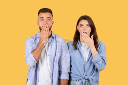 Photo for Man and woman in casual clothing cover their mouths with their hands, displaying expressions of astonishment and surprise against vivid yellow backdrop - Royalty Free Image