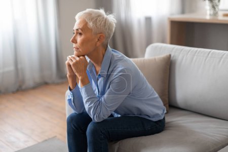 Photo for Depression. Side view of frustrated European senior lady having moment of loneliness and sadness, sitting on couch in modern living room, thinking about problems. Mental health challenges - Royalty Free Image