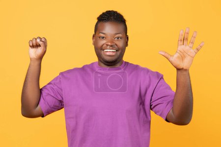 Téléchargez les photos : Un Afro-Américain souriant levant la main montrant le numéro cinq, la paume ouverte cinq doigts et le poing comme zéro sur fond de studio jaune, comptant avec des gestes, souriant à la caméra - en image libre de droit