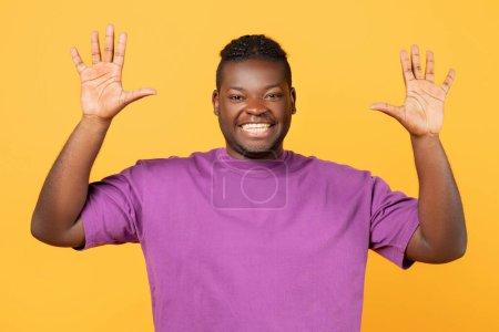 Téléchargez les photos : Joyeux homme afro-américain levant les deux mains montrant le numéro dix, les paumes ouvertes avec cinq doigts debout sur fond jaune, comptant jusqu'à dix, souriant à la caméra - en image libre de droit