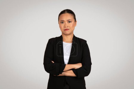 Photo for Professional sad millennial woman in business attire looking skeptical and concerned with arms crossed at work in front of a neutral grey background, studio. Business choice - Royalty Free Image