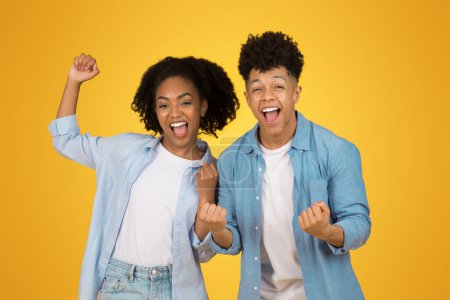 Photo for Two glad exuberant young people celebrate with raised fists and bright smiles, radiating joy and victory against a lively yellow background. Love, relationship, success, win - Royalty Free Image
