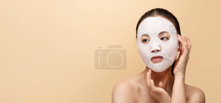 Téléchargez les photos : Femme nue chinoise millénaire joyeuse avec masque cosmétique, profiter du traitement, isolé sur fond beige, studio, panorama, gros plan. Soins de beauté naturels, levage, spa hydratant - en image libre de droit
