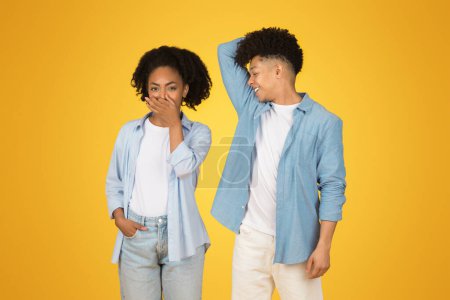 Photo for A young woman covers her mouth in shock while a young man scratches his head in confusion, both displaying humorous expressions of surprise and bewilderment against a yellow backdrop - Royalty Free Image