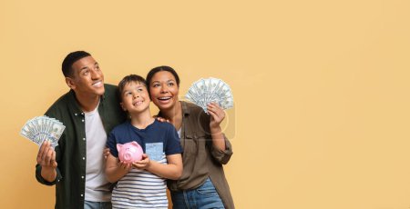 Photo for Family savings, budget planning, childrens pocket money. Positive loving young black father mother and preteen kid son holding cash dollar banknotes and piggy bank, looking at copy space, banner - Royalty Free Image