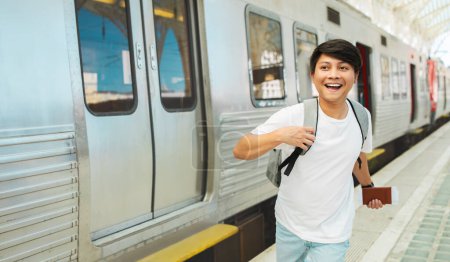 Photo for Excited asian guy tourist with passport and tickets in his hand running by train station, catching his train, carrying his backpack, panorama with copy space. Tourism, travelling, transportation - Royalty Free Image