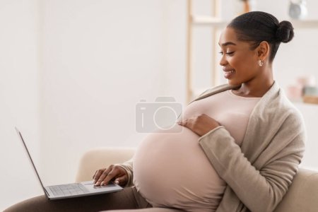 Photo for Pregnant african american lady relaxing at home with computer laptop, sitting on couch in living room, reading pregnancy blog, buying stuff for baby online, side view, copy space - Royalty Free Image