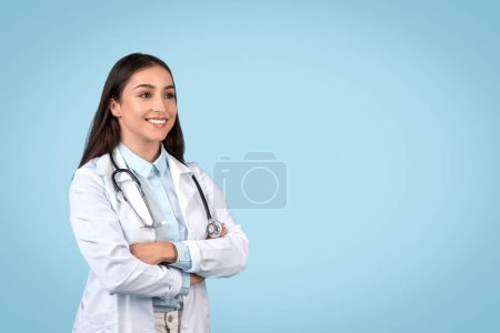 Photo for Happy young physician woman looking aside at free space posing with stethoscope standing in studio over blue background. Medical career concept - Royalty Free Image