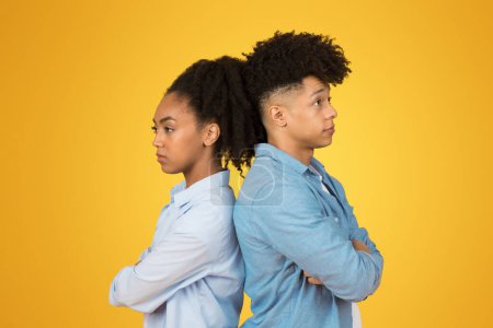 Photo for Sad angry millennial african american man and lady stand back-to-back with arms crossed and displeased expressions, against a vibrant yellow background. Love, relationship problems - Royalty Free Image