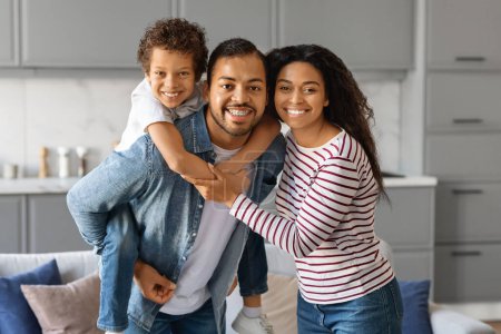 Téléchargez les photos : Portrait d'une heureuse famille afro-américaine de trois personnes posant ensemble à la maison, aimant les jeunes parents noirs et leur petit fils étreignant et souriant à la caméra, appréciant le temps passé ensemble, copiant l'espace - en image libre de droit