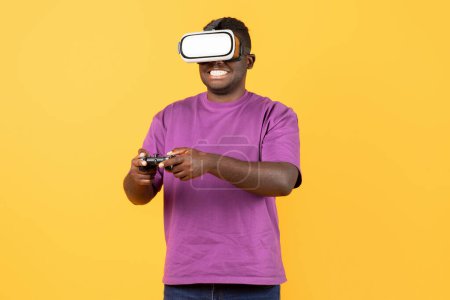 Foto de Chico negro emocionado inmerso en el juego de realidad virtual con auriculares VR, divertirse mientras se involucra con el entretenimiento digital innovador sobre fondo amarillo. Captura de estudio - Imagen libre de derechos