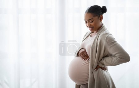 Foto de Sensación de conexión con el feto. Feliz embarazada joven negro tocando su vientre, fondo blanco ventana con espacio vacío, panorama - Imagen libre de derechos