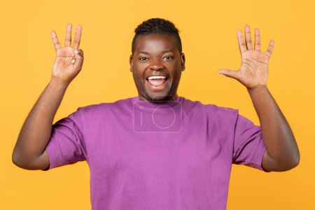 Téléchargez les photos : Homme noir joyeux en t-shirt violet levant les deux mains montrant le numéro huit, paumes ouvertes avec trois et cinq doigts sur fond jaune studio, comptant jusqu'à huit, souriant à la caméra - en image libre de droit