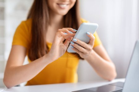 Photo for Closeup Shot Of Young Smiling Woman Sitting At Desk And Using Smartphone, Unrecognizable Female Holding Mobile Phone In Hands, Messaging Or Browsing Application, Cropped Image With Selective Focus - Royalty Free Image