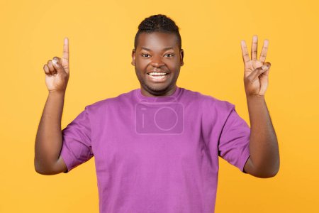 Téléchargez les photos : Dentiste noir levant les deux mains montrant le numéro quatre, gesticulant un et trois doigts sur fond jaune studio, comptant jusqu'à quatre avec des gestes et souriant à la caméra - en image libre de droit