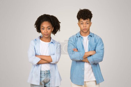 Photo for An African American young woman and man stand side-by-side with their arms crossed, displaying confident stances and slightly skeptical expressions on a clean background - Royalty Free Image