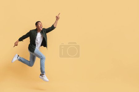 Photo for Great offer, deal. Happy stylish millennial black guy running towards copy space and gesturing, pointing at mockup blank space for advertisement, isolated on beige studio background - Royalty Free Image