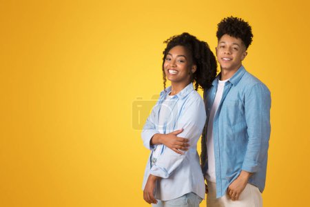 Téléchargez les photos : Un jeune couple noir joyeux en denim décontracté se tient dos à dos avec les bras croisés, souriant en toute confiance sur un fond jaune vif, studio, regardez l'espace libre - en image libre de droit
