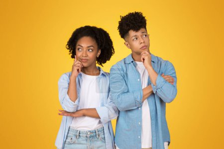 Photo for Two pensive thoughtful African American siblings in casual denim attire stand side by side, lost in thought with curious expressions, think, against a bright yellow background - Royalty Free Image