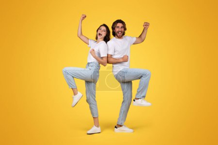 Photo for Cheerful young european guy and woman in white t-shirt celebrate win, success, have fun, rise fists, isolated on orange background studio. Positive winner lifestyle, victory and relationship - Royalty Free Image