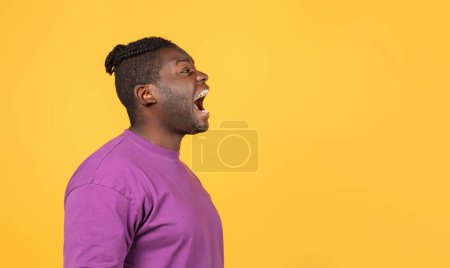 Photo for Side view of mad african american guy in purple t-shirt shouting looking aside at empty space over yellow studio backdrop, panorama. Profile portrait of man screaming expressing negative emotions - Royalty Free Image