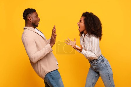 Téléchargez les photos : Conflit vif capturé avec l'homme noir et la femme gesticulant passionnément l'un à l'autre, leurs expressions intenses sur fond jaune vif - en image libre de droit