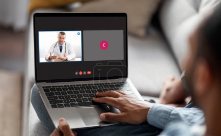 Photo for Black man sitting on couch at home, using laptop computer, have video call with his doctor. African american guy have online appointment with general practitioner, getting prescription. Telemedicine - Royalty Free Image