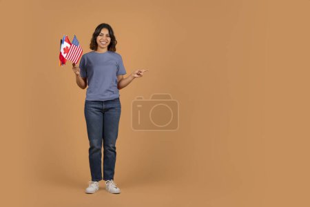 Foto de Alegre joven mujer de Oriente Medio sosteniendo banderas de diferentes países y apuntando a la maqueta espacio de copia para publicidad, fondo colorido. Educación en el extranjero, intercambio de estudiantes - Imagen libre de derechos