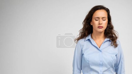 Photo for A contemplative caucasian young woman with closed eyes and curly hair wearing a light blue shirt embodies a moment of serene introspection or possible stress relief, studio - Royalty Free Image