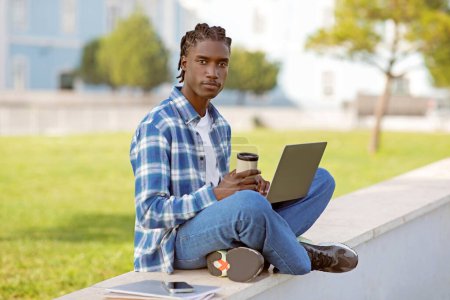 Photo for African american student guy with laptop and takeaway coffee sitting in park, browsing e-learning website for youth pursuing college degrees, enjoying online education and distance learning - Royalty Free Image