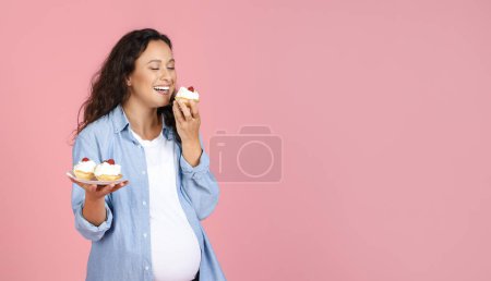 Foto de Hungry Expectant Lady comiendo dulces de pie sobre el fondo de Pink Studio. Alimentos que se deben evitar durante el concepto de embarazo. Panorama, Espacio vacío - Imagen libre de derechos